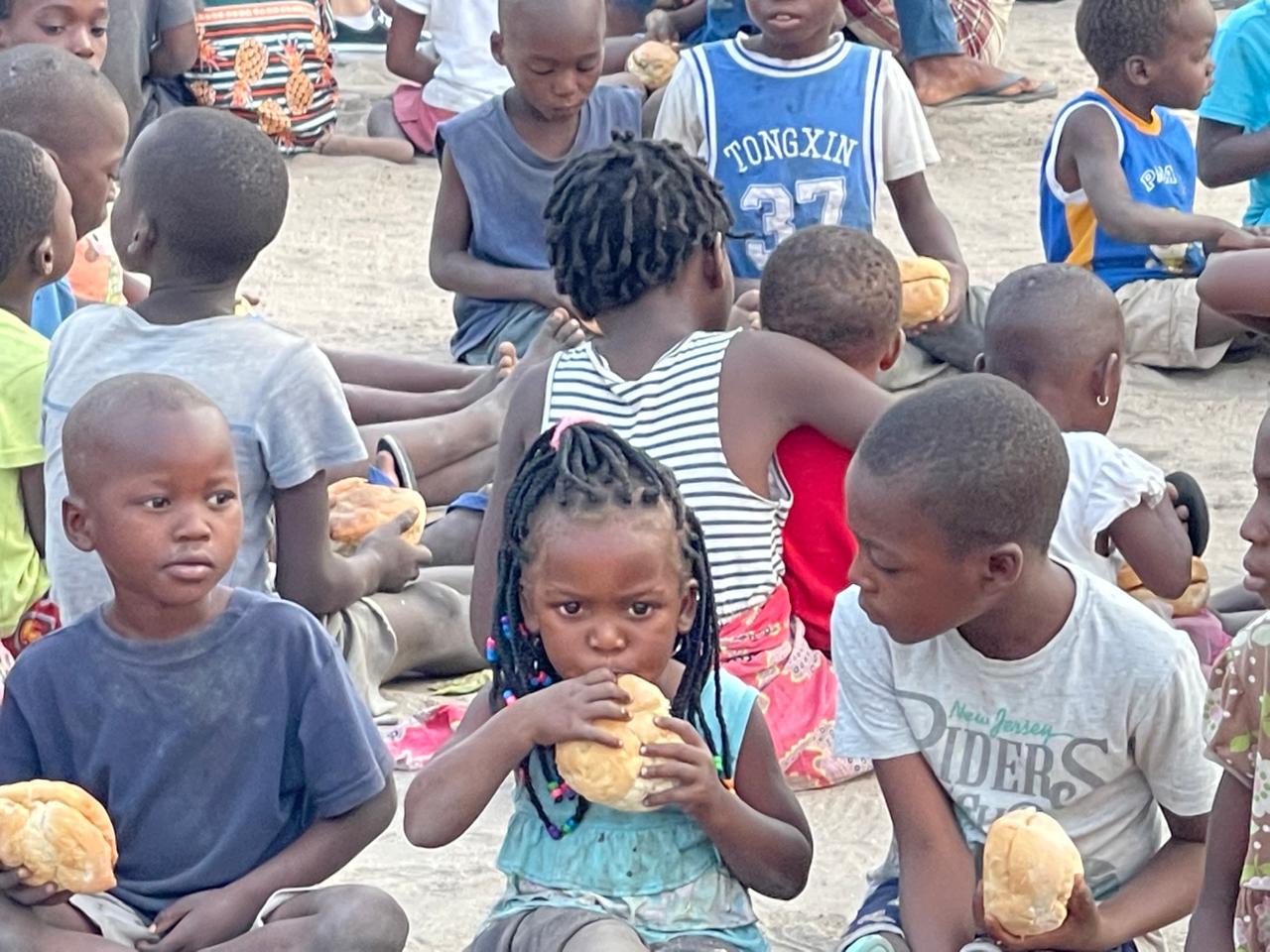 Crianças sentadas na areia segurando os pães recebidos durante uma ação na África